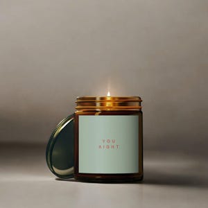 May include: A brown glass candle jar with a gold lid and a white label that reads "YOU AIGHT" in red text. The candle is lit.