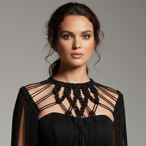 May include: A black dress with a strapless design, paired with a black macrame cape. The cape features a detailed neckline and long fringe that drapes over the shoulders and arms. The dress and cape create an elegant, formal look.