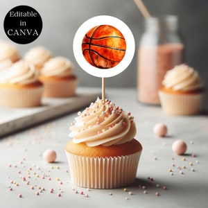 May include: A cupcake with pink and white sprinkles topped with white frosting. A round sticker with a basketball design is attached to a toothpick and inserted into the cupcake.