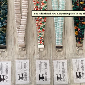 May include: Five fabric lanyards with key rings, each with a unique pattern. Patterns include floral, solid cream, Christmas-themed, light blue gingham, and dark floral. Each lanyard has a metal clasp and key ring. The text "See Additional RPC Lanyard Option in my Shop" is visible.