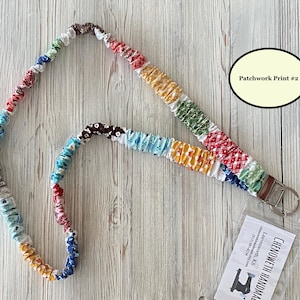 Puede incluir: Un cord&oacute;n de patchwork colorido con un cierre de metal y un llavero. La tela es una mezcla de patrones y colores, incluyendo rojo, azul, amarillo y verde. El texto "Patchwork Print #2" est&aacute; en un &oacute;valo color crema. El cord&oacute;n est&aacute; sobre un fondo de madera clara.