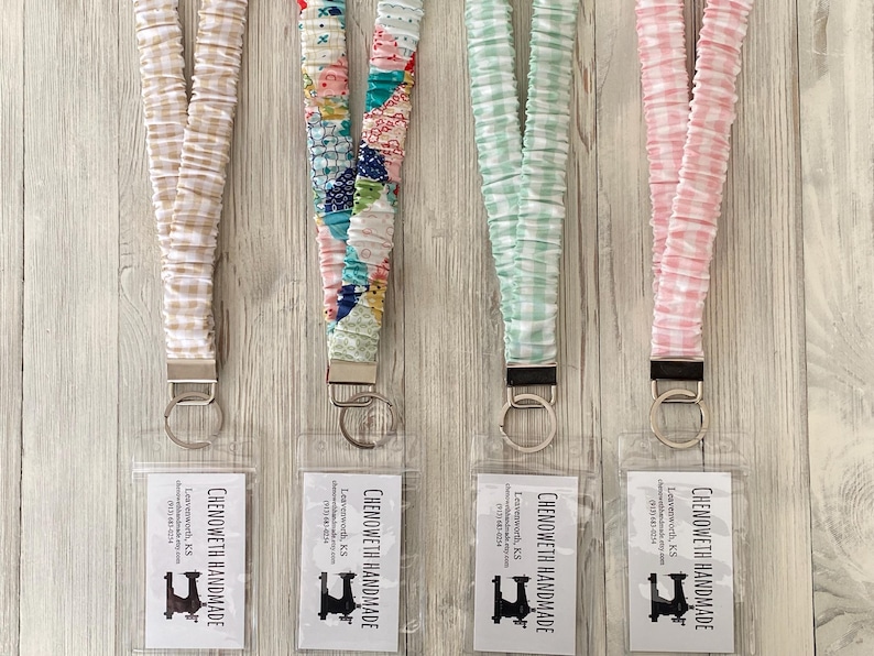 Puede incluir: Cuatro cordones de tela con diferentes patrones y colores, cada uno con un cierre de metal y un tarjetero de pl&aacute;stico transparente. Los cordones son beige, patchwork, verde menta y cuadros rosas. Cada tarjetero tiene el texto "CHENOWETH HANDMADE".