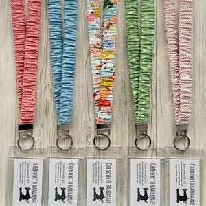 May include: Five fabric lanyards in pink, blue, patterned, green, and pink with white polka dots. Each lanyard has a metal clasp and a clear plastic holder. The text "CHENOWETH HANDMADE" is visible on the clear plastic holders.