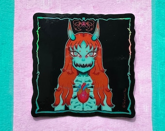 May include: A holographic sticker featuring a teal-colored demon with red hair and horns, holding a red heart in its chest. The demon has a skeletal ribcage and a toothy grin. The sticker has a black background and a glittery border.