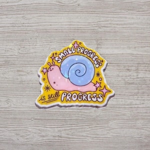 May include: A yellow sticker featuring a cartoon snail with a pink body and a blue shell. The text "SMALL PROGRESS is still PROGRESS" is written on the sticker, with star details.