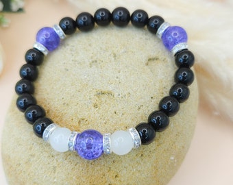 Puede incluir: Un brazalete de cuentas negras con dos cuentas moradas y dos blancas. Las cuentas están adornadas con pequeños diamantes de imitación plateados.