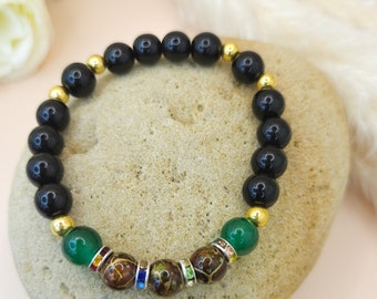 May include: Black and green beaded bracelet with gold accents. The bracelet features a brown bead with colorful rhinestones.