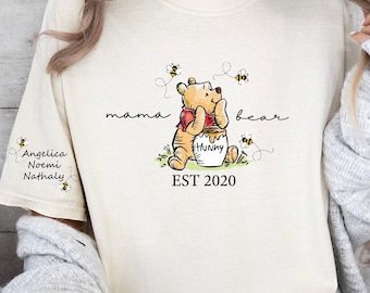 May include: A cream-colored t-shirt with a cartoon image of Winnie the Pooh holding a honey pot. The text "mama bear" is written above the image and "EST 2020" is written below the image.