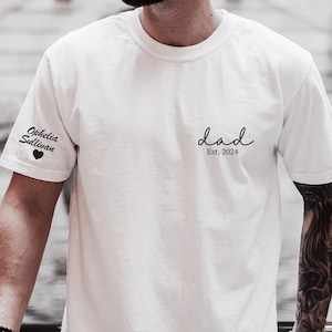 Peut inclure: T-shirt blanc avec le texte "dad Est. 2024" sur le devant et le texte "Ophelia Sullivan" sur la manche gauche avec un petit cœur.