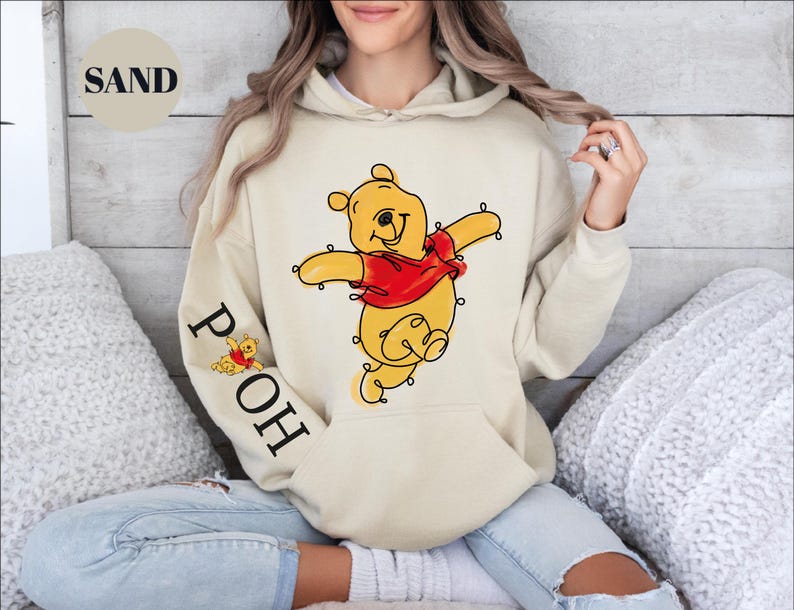 A woman wearing a hooded sweatshirt with a Winnie the Pooh character printed on it, sitting on a couch.