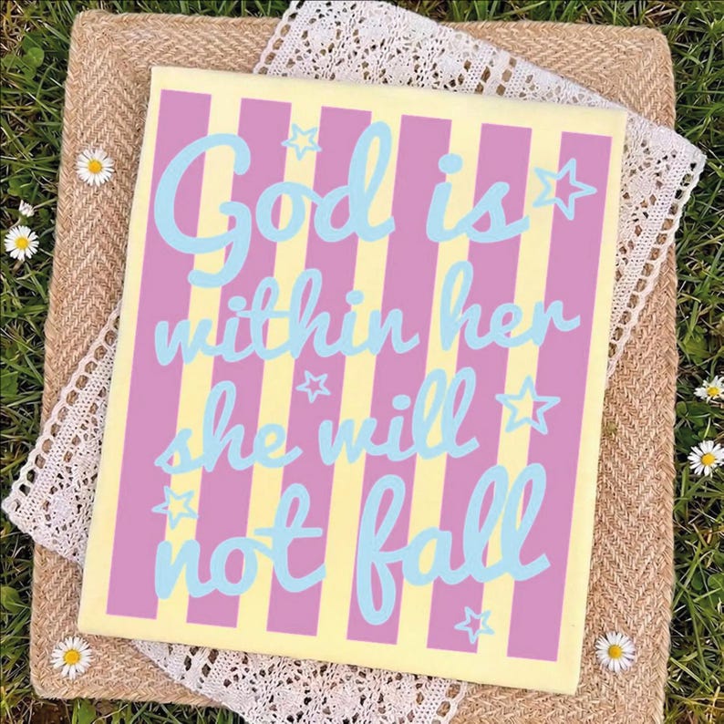 A colorful sign with the text "God is within her she will not fall" is displayed on a straw mat with white flowers.