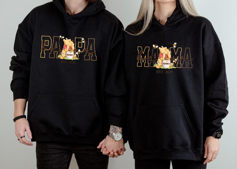Two people wearing black hooded sweatshirts with the text "PAPA" and "MAMA" printed on them.