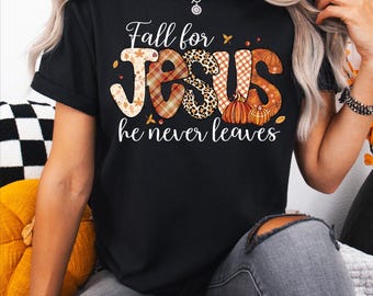 May include: Black t-shirt with the text "Fall for JESUS he never leaves". The word JESUS is in a plaid, leopard print, and pumpkin design. The shirt is a fall-themed design.