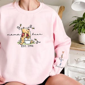 a woman sitting on a bed wearing a pink winnie the pooh sweatshirt