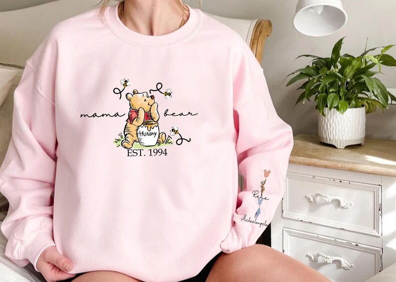 a woman sitting on a bed wearing a pink winnie the pooh sweatshirt