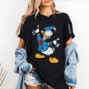 A woman wearing a black t-shirt with a cartoon image of a duck, a denim jacket, and denim shorts.