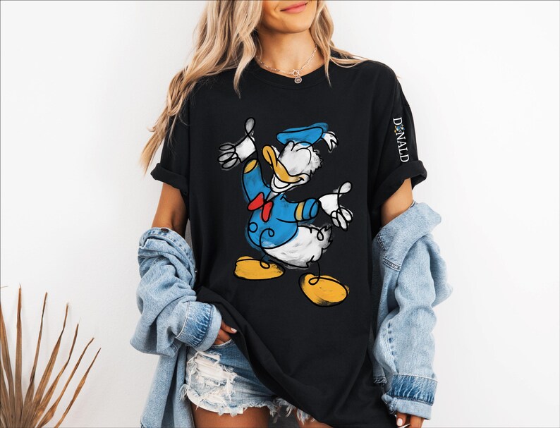 A woman wearing a black t-shirt with a cartoon image of a duck, a denim jacket, and denim shorts.