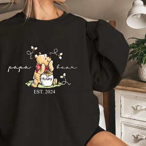 a woman is holding a black shirt with a picture of winnie the pooh on