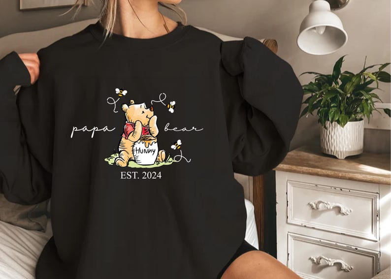 a woman is holding a black shirt with a picture of winnie the pooh on