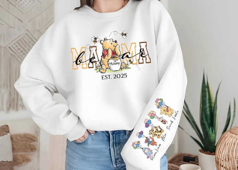 A person wearing a white sweatshirt with a Winnie the Pooh-themed design, including the character's name and the year 2015.