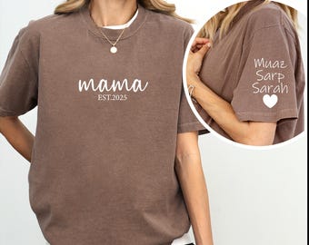 May include: A brown t-shirt with the text "mama est. 2023" on the front. The back of the shirt has the text "Muaz Sarp Sarah" and a heart.