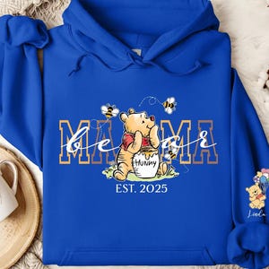 A blue hoodie with a Winnie the Pooh design and the text "MAMMA" printed on it, along with a small Winnie the Pooh character.