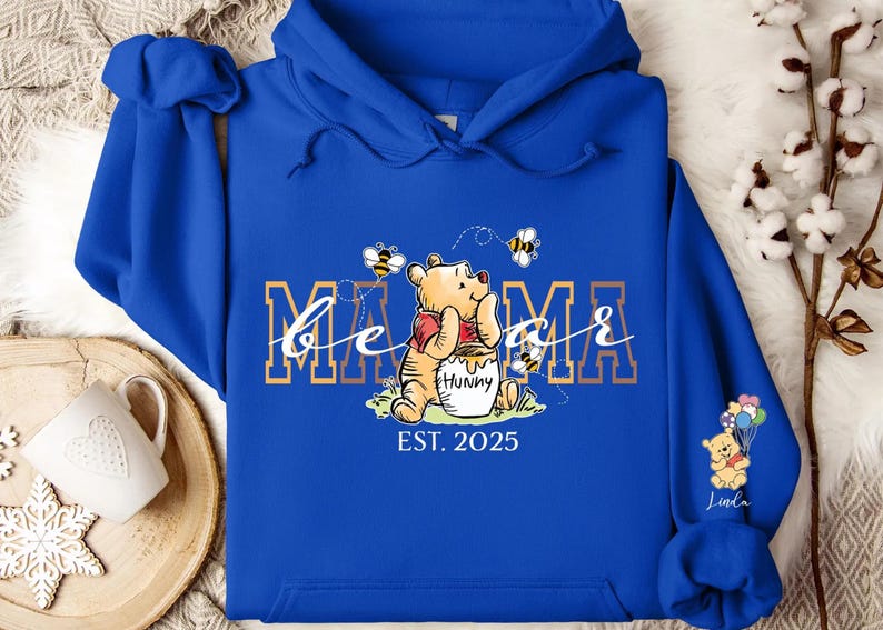 A blue hoodie with a Winnie the Pooh design and the text "MAMMA" printed on it, along with a small Winnie the Pooh character.