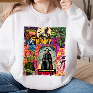 May include: White sweatshirt featuring a colorful graphic of classic movie monsters. The design includes images of the Wolfman, Mummy, Creature from the Black Lagoon, Dracula, Frankenstein, and the Invisible Man. Text includes "Mummy Like That" and "I Never Drink Wine".