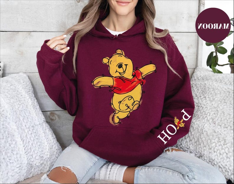 A woman wearing a red hoodie with a cartoon image of Winnie the Pooh on it, sitting on a couch.
