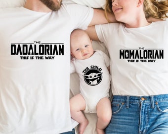 May include: A white t-shirt with the text "The Dadalorian This is the Way" in black. A white t-shirt with the text "The Momalorian This is the Way" in black. A white onesie with the text "The Child" and a black and white image of a character from the Star Wars series.