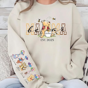 A person wearing a white sweatshirt with a Winnie the Pooh-themed design, including the character's face and the text "Mama" and "Est. 2025".