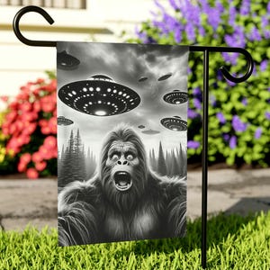 May include: A black and white garden flag featuring a screaming Bigfoot with multiple flying saucers in the background.