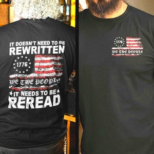 Peut inclure: T-shirts noirs avec des motifs patriotiques. L'un des t-shirts présente un drapeau américain vieilli avec le texte "1776" et "WE THE PEOPLE". L'autre t-shirt porte le texte "IT DOESN'T NEED TO BE REWRITTEN" et "IT NEEDS TO BE REREAD" avec un motif de drapeau.