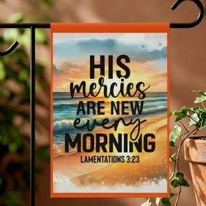 Peut inclure: Un drapeau de jardin rectangulaire avec une bordure orange affiche le texte "HIS mercies ARE NEW every MORNING" sur une scène de plage à l'aquarelle. Le drapeau est suspendu à un support en métal noir, avec une plante en pot en arrière-plan.