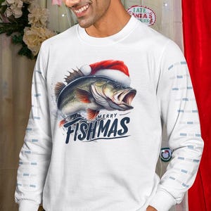 May include: White long-sleeve shirt with a graphic of a fish wearing a Santa hat. The fish is jumping out of the water with the text "MERRY FISHMAS" in navy blue. The sleeves have a light blue square pattern.
