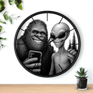 May include: Black and white wall clock featuring a smiling Bigfoot and an alien taking a selfie. The clock has a black frame and hands, with a white background. The image includes a forest scene.
