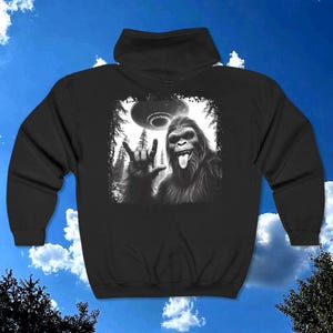 May include: Black hooded sweatshirt with a graphic print of a Bigfoot giving the peace sign with a UFO in the background.