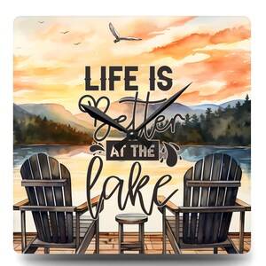 May include: Square wall clock with a scenic lake view and the text "LIFE IS Better AT THE lake." The clock face features two wooden Adirondack chairs, a small table, and a watercolor sunset with mountains and a flying bird.