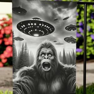 May include: A black and white garden flag depicting a large, hairy, ape-like creature with a wide-open mouth, looking up in fear at a fleet of flying saucers. The creature is in a woodland setting.