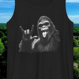 May include: Black tank top with a graphic of a smiling Bigfoot giving the 'I love you' hand sign.