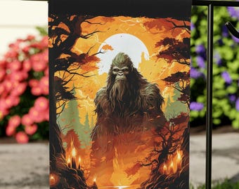 May include: A garden flag featuring a Bigfoot illustration. The design shows a large, hairy Bigfoot in a forest scene, set against a full moon and a warm colour scheme of orange, brown, and yellow. The flag is displayed outdoors.