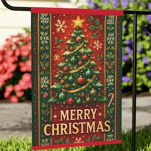 May include: A rectangular Christmas garden flag with a red border and a festive design. The flag features a decorated Christmas tree with ornaments and a star, snowflakes, and the words "MERRY CHRISTMAS" in gold lettering. The flag is hanging on a black metal stand.