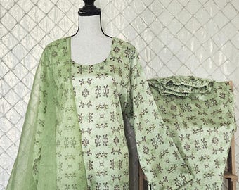 May include: A light green two-piece outfit with a matching sheer scarf. The outfit features a floral pattern in brown and green. The top has long sleeves and a round neckline. The pants are straight-legged.