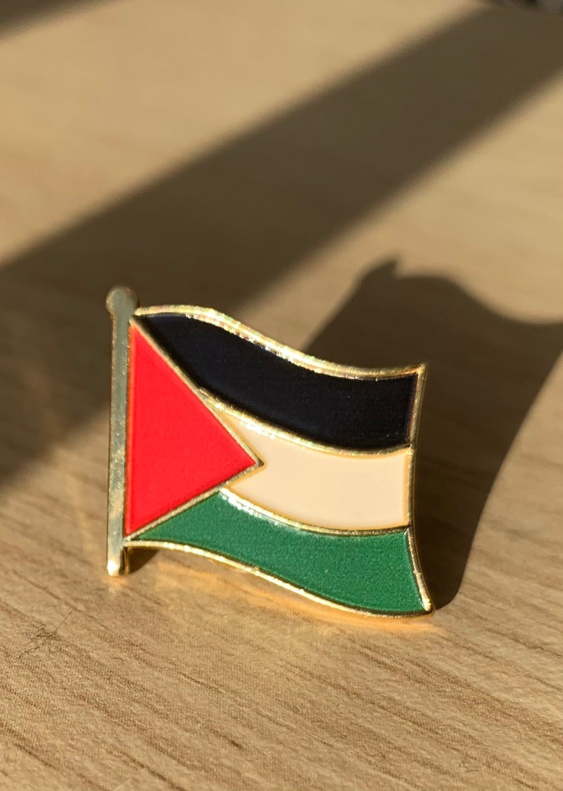 Pu&ograve; includere: Uno spillo dorato con un designo di bandiera palestinese in rosso, nero, bianco e verde.
