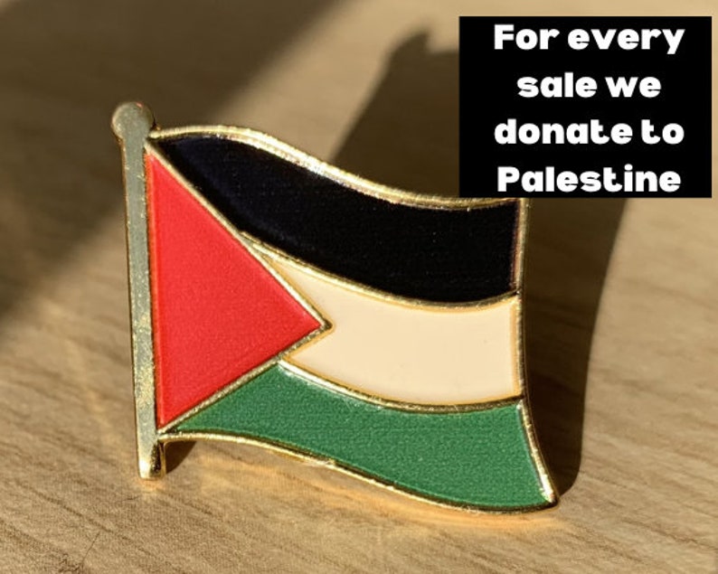 Pu&ograve; includere: Uno spillo dorato con un designo di bandiera palestinese. La bandiera &egrave; rossa, bianca, nera e verde. Il testo "Per ogni vendita doniamo alla Palestina" &egrave; visibile sullo sfondo.