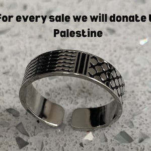 May include: A silver ring with a black and white geometric design. The ring is made of metal and has a smooth finish.