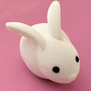 May include: A white plush bunny with black eyes. The bunny is lying on its side with its head turned to the right.