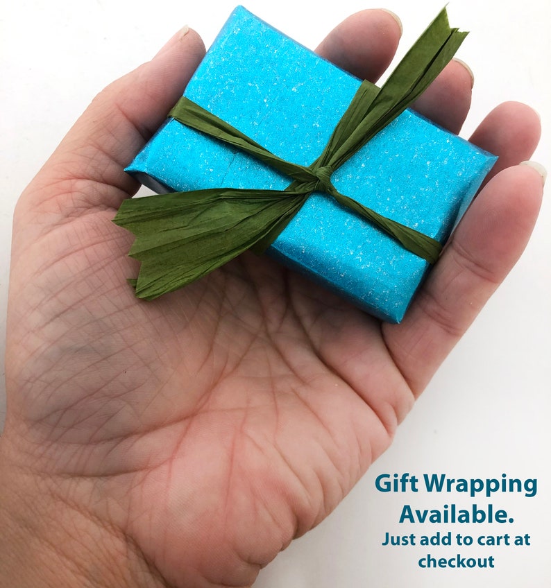 May include: A small, blue gift box with a green ribbon tied in a bow. The text "Gift Wrapping Available. Just add to cart at checkout" is printed below the box.