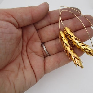 May include: A pair of gold wheat-shaped earrings with thin wire loops. The earrings are made of metal and have a textured surface.