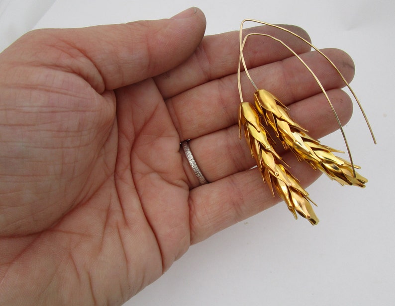 May include: A pair of gold wheat-shaped earrings with thin wire loops. The earrings are made of metal and have a textured surface.